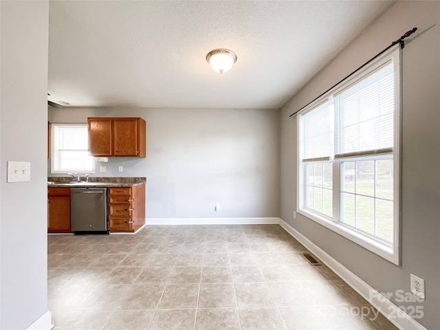 kitchen with stainless steel dishwasher, light tile patterned floors, a textured ceiling, and sink