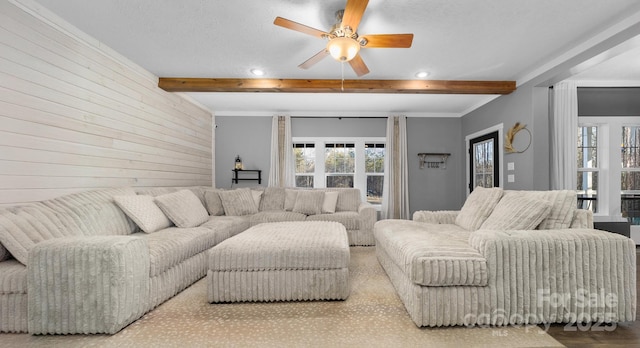 living room featuring beam ceiling, ceiling fan, and wooden walls