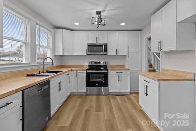 kitchen with white cabinets, stainless steel appliances, butcher block counters, and sink