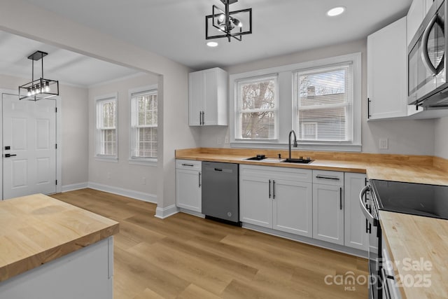 kitchen featuring wood counters, white cabinetry, hanging light fixtures, and appliances with stainless steel finishes