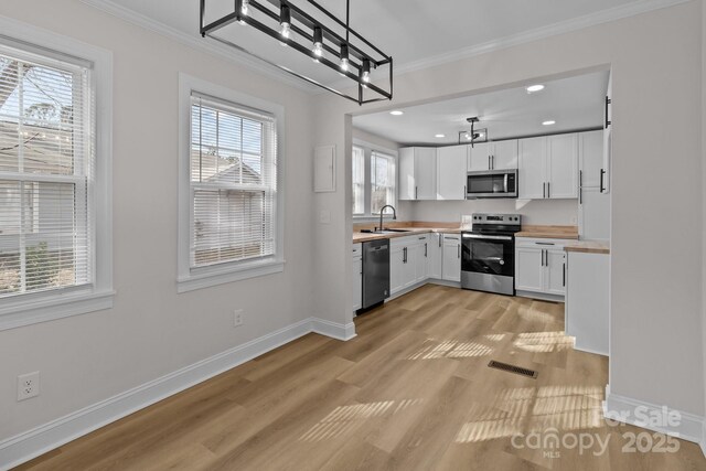 kitchen with wood counters, light hardwood / wood-style floors, pendant lighting, white cabinets, and appliances with stainless steel finishes