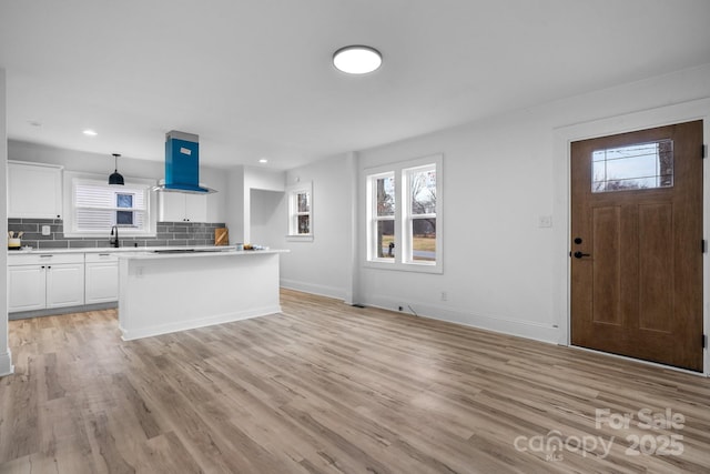 kitchen with wall chimney exhaust hood, a kitchen island, tasteful backsplash, light hardwood / wood-style floors, and white cabinetry