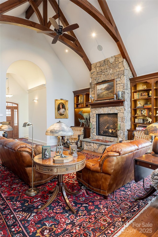 living room with a stone fireplace, hardwood / wood-style floors, ceiling fan, high vaulted ceiling, and beam ceiling