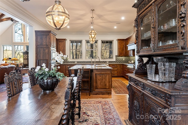 kitchen with decorative light fixtures, an island with sink, tasteful backsplash, dark brown cabinetry, and sink