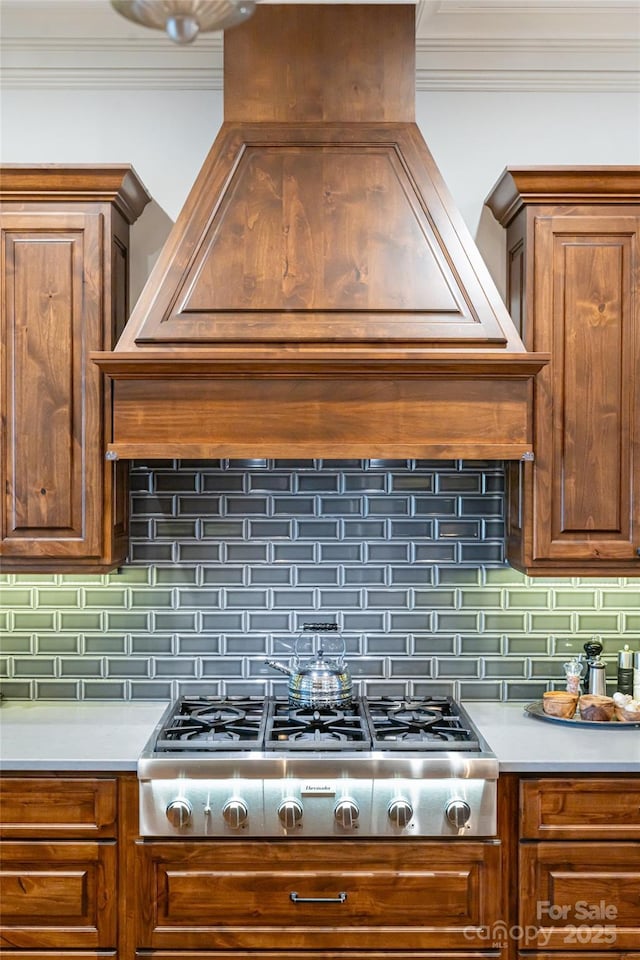 kitchen with stainless steel gas stovetop, crown molding, decorative backsplash, and custom range hood