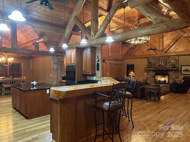 kitchen featuring wooden ceiling, lofted ceiling with beams, ceiling fan with notable chandelier, a stone fireplace, and decorative light fixtures