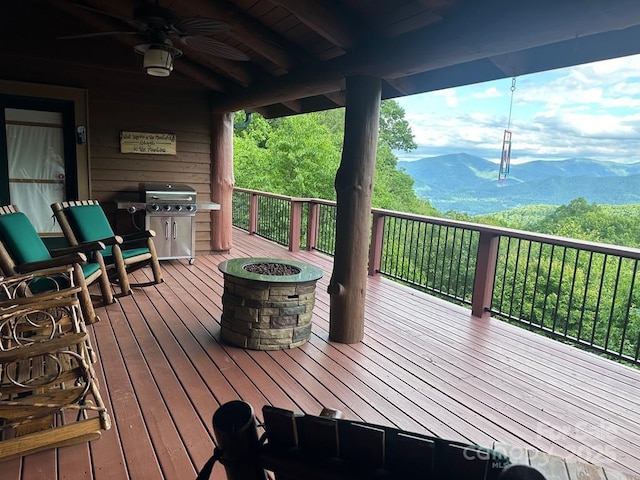 wooden deck featuring a grill, ceiling fan, a mountain view, and an outdoor fire pit