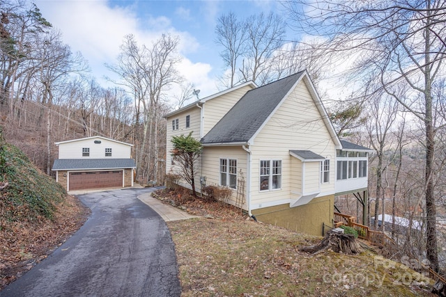 view of property exterior featuring a garage, roof with shingles, and a sunroom