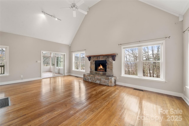 unfurnished living room featuring baseboards, visible vents, a ceiling fan, light wood-style flooring, and a stone fireplace