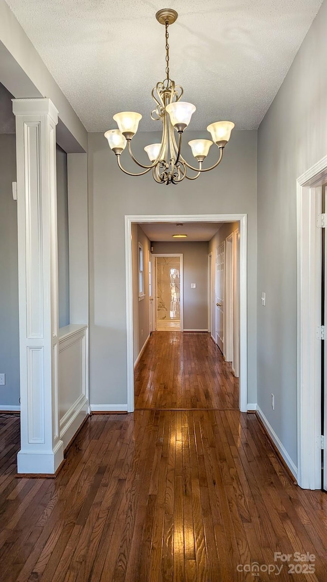 unfurnished dining area with dark hardwood / wood-style flooring, ornate columns, a textured ceiling, and a chandelier