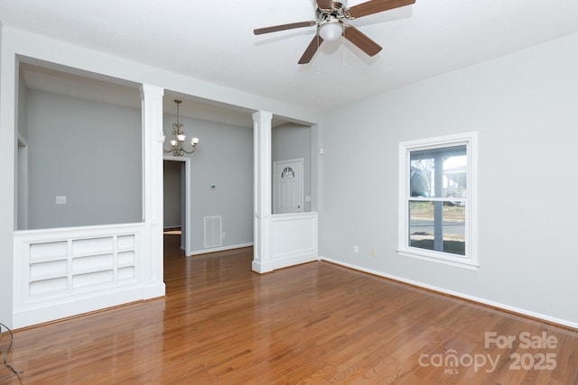 empty room featuring ornate columns, ceiling fan with notable chandelier, and hardwood / wood-style flooring