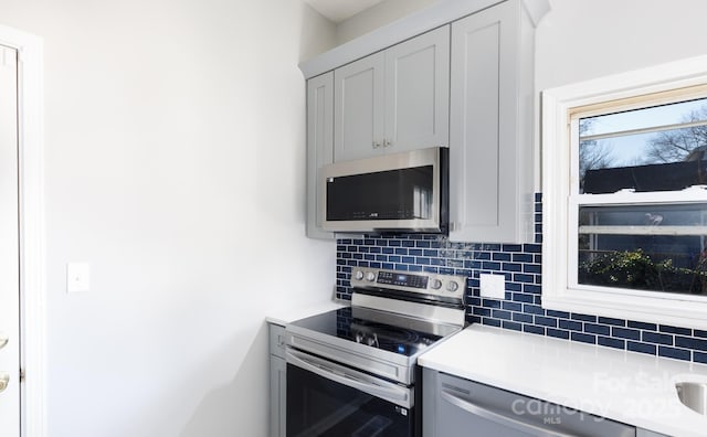 kitchen with gray cabinets, decorative backsplash, and stainless steel appliances