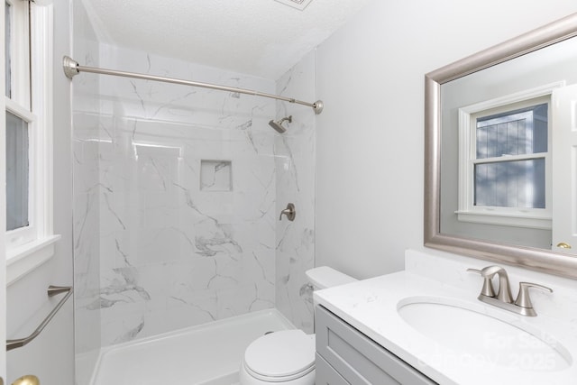 bathroom featuring a textured ceiling, vanity, toilet, and tiled shower