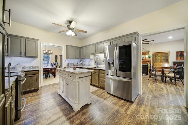 kitchen with ceiling fan with notable chandelier, a center island, light stone counters, stainless steel appliances, and dark wood-type flooring