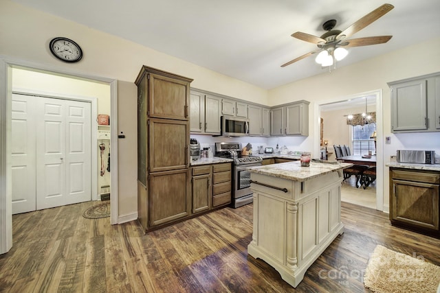 kitchen with gray cabinets, a kitchen island, appliances with stainless steel finishes, dark hardwood / wood-style flooring, and light stone counters