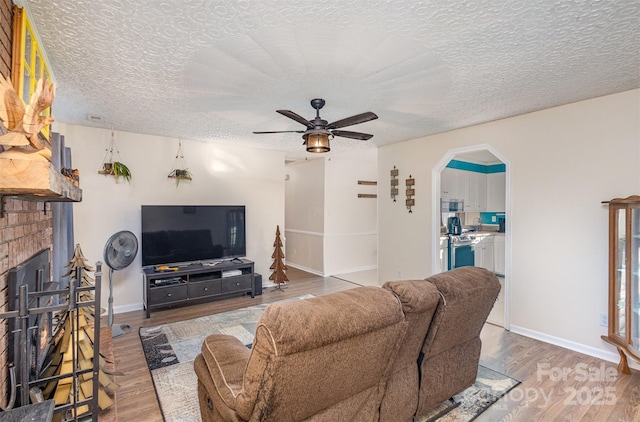 living room featuring hardwood / wood-style floors, a fireplace, ceiling fan, and a textured ceiling