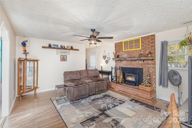 living room featuring ceiling fan, light hardwood / wood-style floors, a wood stove, and a textured ceiling