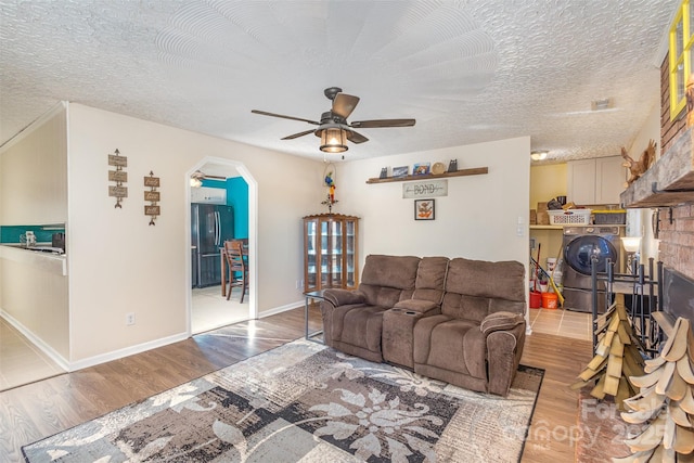 living room with ceiling fan, light wood-type flooring, a textured ceiling, and washer / dryer