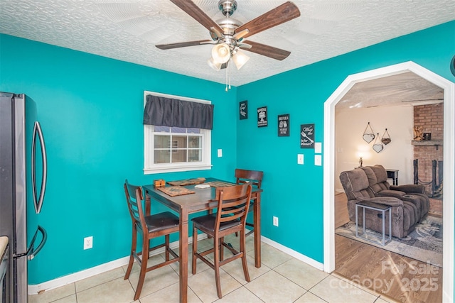 dining area with ceiling fan, a fireplace, light tile patterned floors, and a textured ceiling