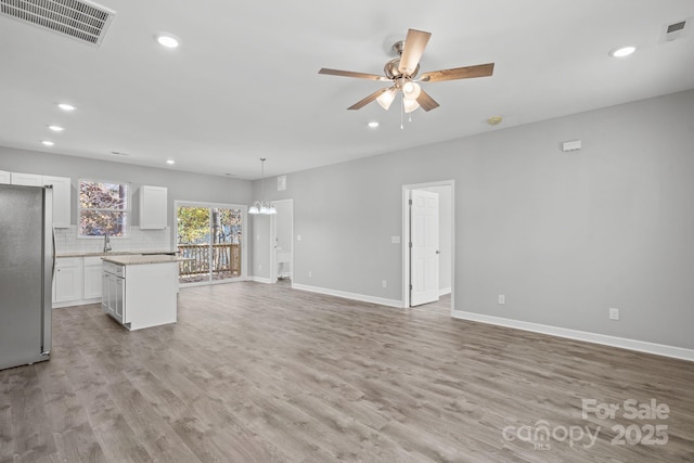 unfurnished living room with ceiling fan with notable chandelier and light hardwood / wood-style flooring