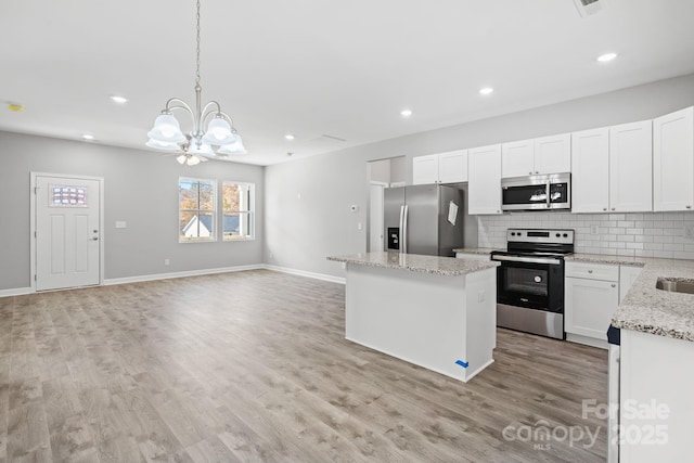 kitchen featuring appliances with stainless steel finishes, decorative light fixtures, white cabinetry, and a kitchen island