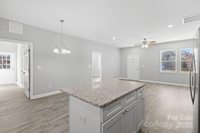 kitchen with a center island, ceiling fan with notable chandelier, stainless steel fridge, light wood-type flooring, and decorative light fixtures