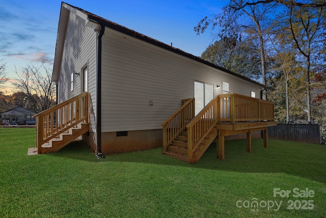 back house at dusk with a wooden deck and a lawn