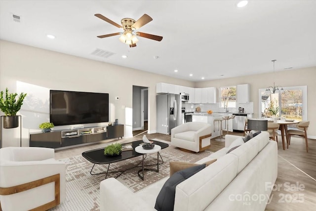 living room with ceiling fan with notable chandelier and light hardwood / wood-style flooring