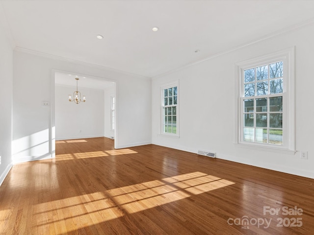 spare room with hardwood / wood-style flooring, ornamental molding, a wealth of natural light, and an inviting chandelier