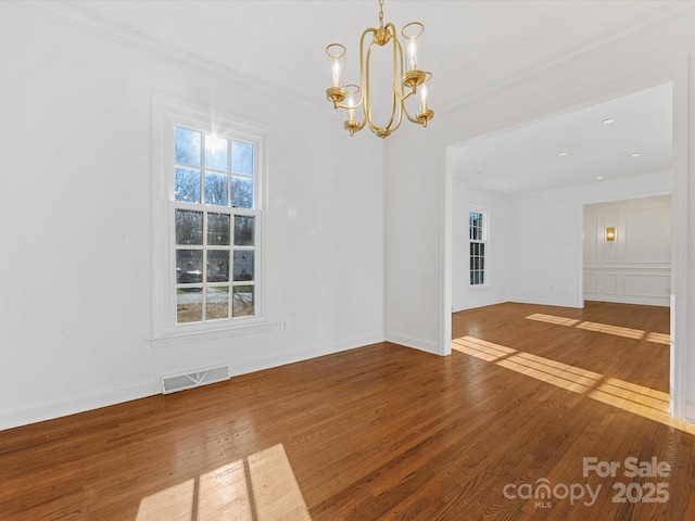 empty room featuring ornamental molding, hardwood / wood-style flooring, and a notable chandelier