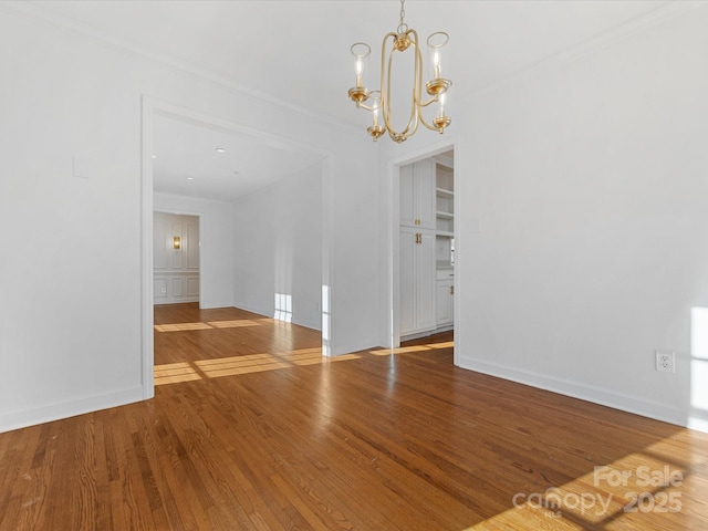 empty room with crown molding, wood-type flooring, and an inviting chandelier