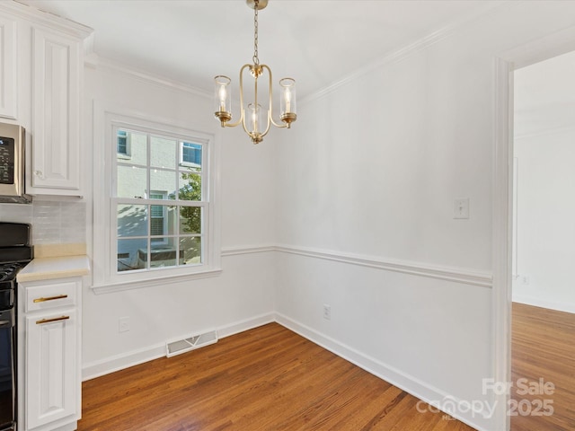 unfurnished dining area with a chandelier, light hardwood / wood-style floors, and ornamental molding