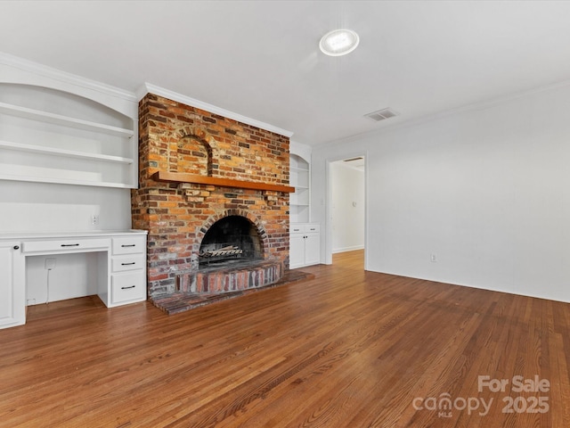 unfurnished living room with built in features, wood-type flooring, ornamental molding, and a brick fireplace