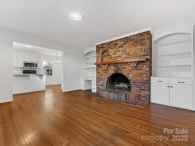 unfurnished living room featuring a chandelier, dark hardwood / wood-style flooring, crown molding, and a brick fireplace