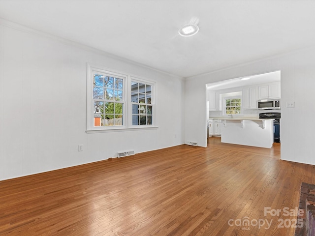 unfurnished living room with plenty of natural light, light wood-type flooring, and crown molding