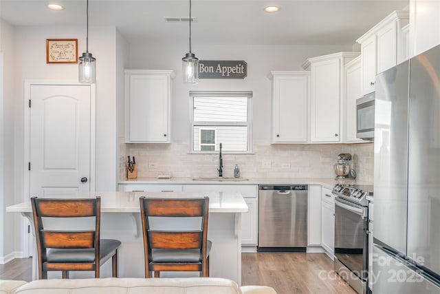 kitchen with pendant lighting, white cabinets, sink, appliances with stainless steel finishes, and a breakfast bar area