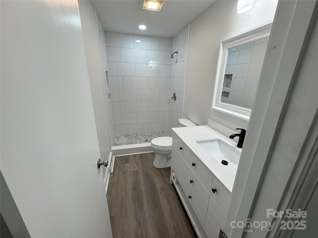 bathroom featuring hardwood / wood-style floors, vanity, toilet, and a tile shower