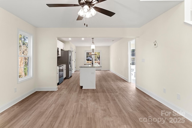 unfurnished living room with a ceiling fan, light wood-type flooring, a sink, and baseboards