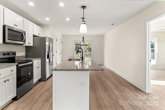 kitchen featuring a sink, white cabinets, appliances with stainless steel finishes, light wood finished floors, and a center island with sink