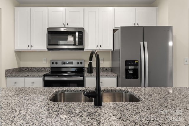 kitchen featuring appliances with stainless steel finishes, a sink, light stone countertops, and white cabinets