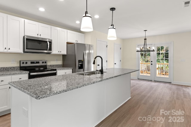 kitchen with white cabinets, an island with sink, light wood-style flooring, stainless steel appliances, and a sink