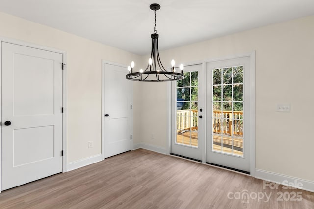 unfurnished dining area with a notable chandelier, baseboards, and wood finished floors