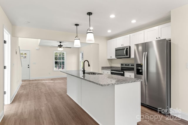 kitchen with light stone counters, a sink, white cabinetry, light wood-style floors, and appliances with stainless steel finishes