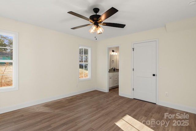 unfurnished bedroom with multiple windows, connected bathroom, baseboards, and wood finished floors