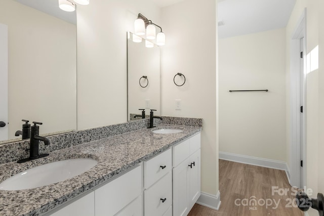 full bathroom with double vanity, wood finished floors, a sink, and baseboards