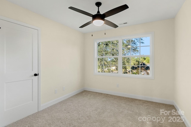 carpeted empty room with visible vents, a ceiling fan, a wealth of natural light, and baseboards