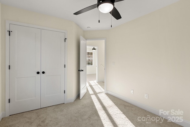 unfurnished bedroom with baseboards, a ceiling fan, a closet, and light colored carpet