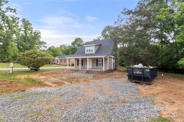 view of front of home with roof with shingles, covered porch, and gravel driveway