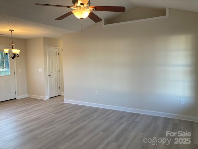 spare room featuring ceiling fan with notable chandelier, light hardwood / wood-style floors, and vaulted ceiling