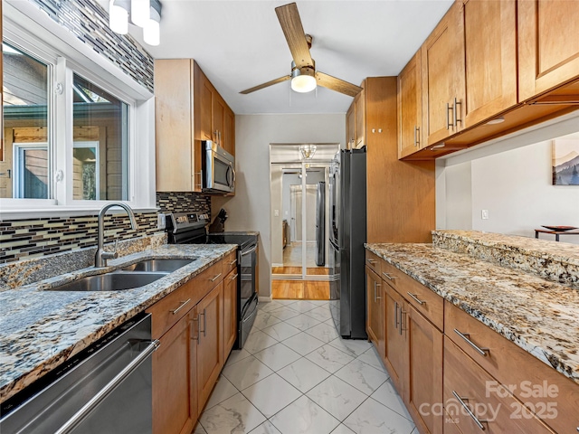 kitchen featuring sink, light stone counters, appliances with stainless steel finishes, ceiling fan, and decorative backsplash